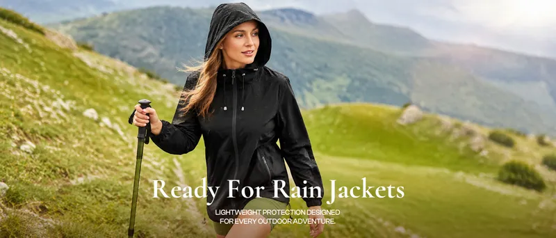 A woman in a black hooded rain shell on a green hillside