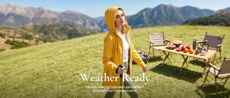 A woman in a yellow hooded shell on a mountain meadow