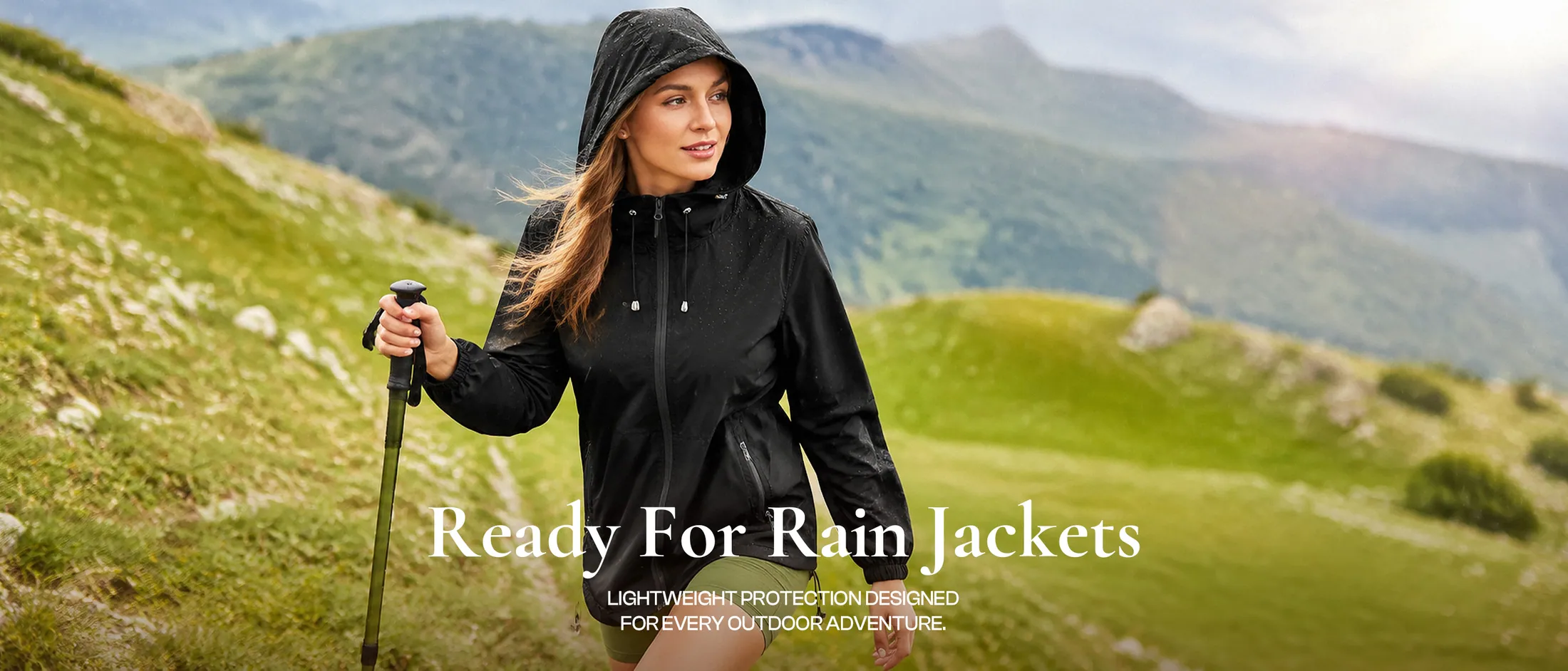 A woman in a black hooded rain shell on a green hillside
